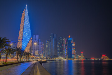 Doha city business downtown center panorama illuminated at night, with modern skyscrapers and sea in the foreground, Qatar