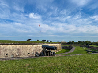 Row of historic cannons positioned along the grassy ramparts of Fort Macon State Park in North Carolina, with the American flag flying proudly above. A powerful image of military history, patriotism, 
