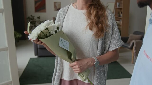 Over shoulder view of African American courier holding bouquet of daises while waiting for woman