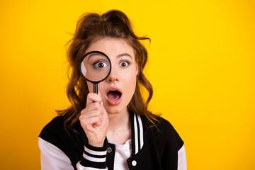 Teenage girl holding a magnifying glass against bright yellow background, exploring curiosity