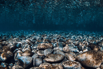 Underwater sea with stone sea bottom and reflection on surface.