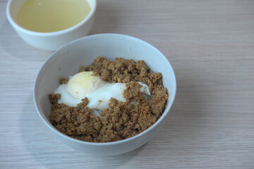 A comfort food bowl with minced meat and a half-boiled egg, a simple and nutritious meal. A small bowl of clear soup is visible in the background, completing a classic Asian meal.