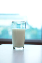 A fresh glass of milk served on a wooden table, set against a bright, clean, out-of-focus background. 