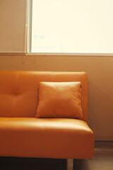 A clean, modern leather sofa in a warm, orange tone with a matching pillow. 