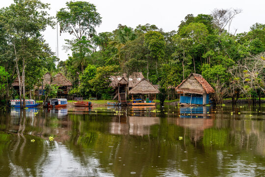 Traditionelle Dorfh&uuml;tten am Flussufer des Amazonas umgeben von Regenwald