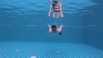 A swimmer glides gracefully underwater, showcasing the vibrant blue tiles of a pool. The serene environment captures the essence of aquatic activities, ideal for relaxation and fitness.