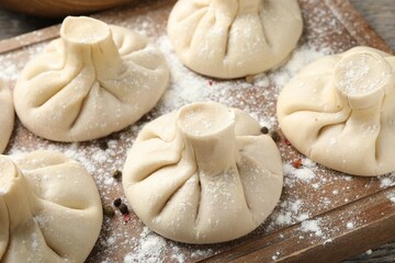 Uncooked khinkalis (dumplings) with peppercorns on wooden board, closeup