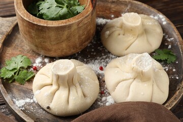 Uncooked khinkalis (dumplings) with peppercorns and parsley on wooden table, closeup