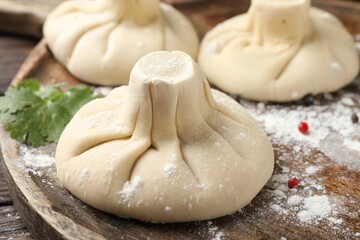 Uncooked khinkalis (dumplings) with peppercorns and parsley on wooden table, closeup