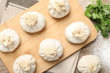 Uncooked khinkalis (dumplings) and cilantro on wooden table, flat lay