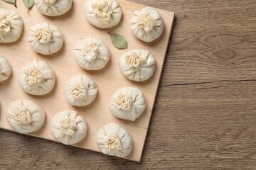 Uncooked khinkalis (dumplings) and bay leaves on wooden table, top view. Space for text