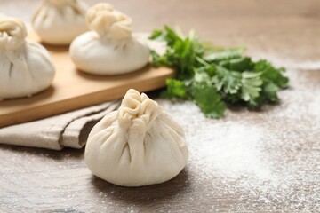 Uncooked khinkalis (dumplings) and cilantro on wooden table, closeup. Space for text