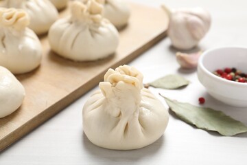 Uncooked khinkalis (dumplings) and spices on white wooden table, closeup