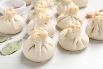 Uncooked khinkalis (dumplings) and spices on white wooden table, closeup