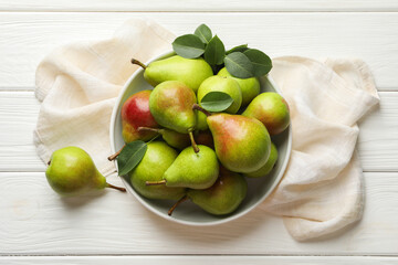 Fresh ripe pears in bowl and green leaves on white wooden table, top view