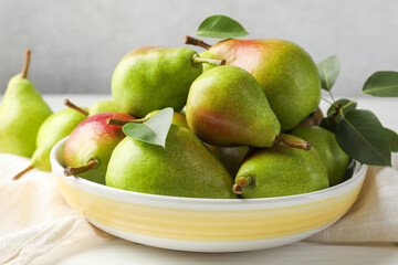 Fresh ripe pears in bowl and green leaves on white wooden table, closeup