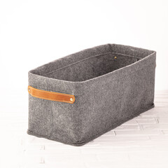 A gray felt storage basket with sturdy leather handles sits on a surface, perfect for organizing...