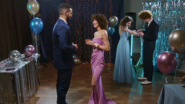 Group of two happy couples in formal clothes talking and giving each other compliments during prom night