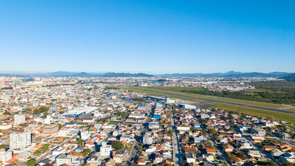 Fototapeta premium Aerial view of Navegantes Airport runway surrounded by city buildings on a sunny day.