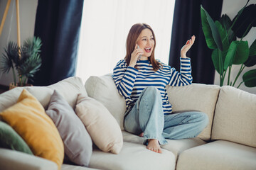 Obraz premium Young woman enjoying a phone call in a cozy living room with vibrant decor and stylish casual attire, relaxed at home