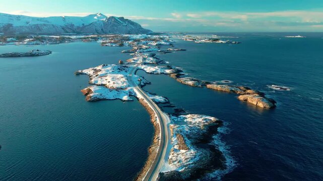 aerial drone shot captures the iconic Atlantic Ocean Road Atlanterhavsveien in Norway during winter, with the road and surrounding islets covered in pristine snow, contrasting beautifully with the dee