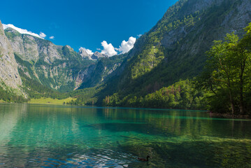 Beautiful Königssee lake in Bavaria, Germany – turquoise alpine water surrounded by majestic mountains and lush forest under clear summer sky.