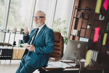 Confident senior businessman with a beverage in his modern office, enjoying a reflective moment...
