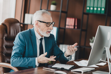 Senior businessman working attentively on a computer in an office setting wearing a blue suit