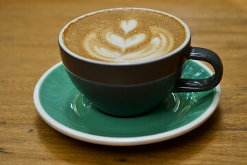 Old fashioned cappuccino cup  with one heart shape on the coffea foam on a green plate.