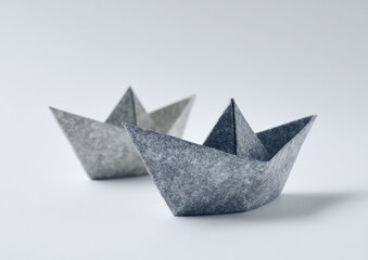 Two gray origami paper boats on a white background