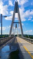 Fototapeta premium A modern cable-stayed bridge spans a road, reflecting the vibrant sky in a puddle below.