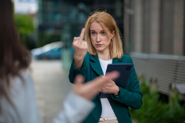 Serious businesswoman holding tablet and showing middle finger gesture outdoors in urban...