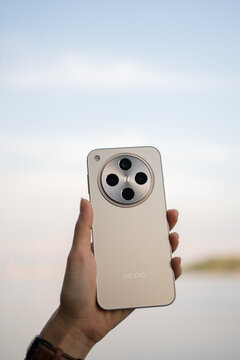 PENANG, MALAYSIA - JAN 02, 2025: Close-up of a hand holding an OPPO Find X8 smartphone showing large circular Hasselblad camera module against a soft sky and water background.