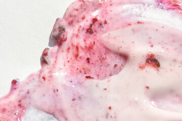 close up of swirled pink and white yogurt with fruit chunks and smooth texture on white background.