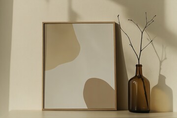 A picture frame hangs on a wall beside a vase of dried flowers