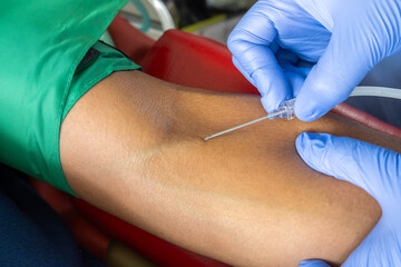 Close-up of gloved medical professional inserting a needle into a patient’s arm for blood draw,...