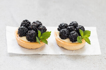 Two Mini blackberry round tartlets. On paper. Light gray background. Close up
