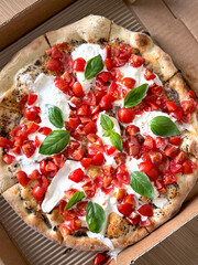 Italian pizza with fresh burrata cheese, cherry tomatoes and basil leaves in a delivery box. Top...