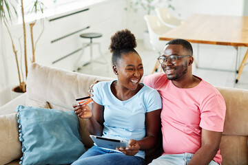 portrait of happy smiling young couple using a tablet computer and a credit card  for online shopping at home, technology and internet use in everyday life concept