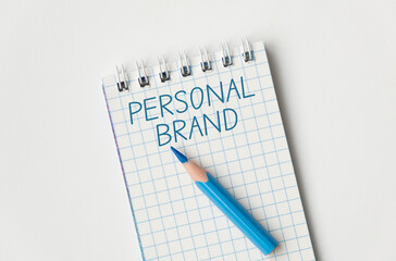 A blue pencil is on a notebook with the word Personal Brand written in blue