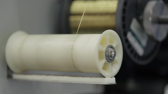 Close up of plastic spool with thin industrial wire winding on modern production equipment. Concept of manufacturing process, precision technology, machinery, factory automation and engineering. - Powered by Adobe