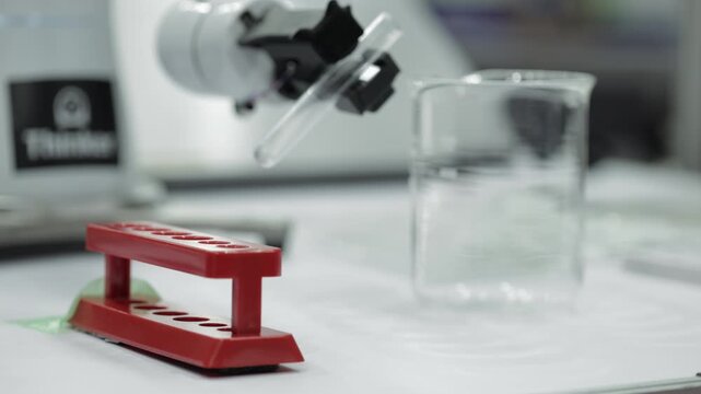 Ai Robotic system pouring liquid from test tube into glass beaker and placing empty tube on holder. Concept of automated laboratory research, biotechnology, pharmacy and clinical analysis