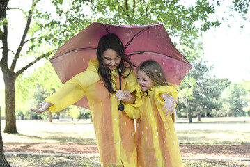 Portrait of joyful children spending time outside standing with an umbrella in the rain.
