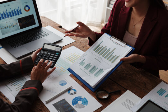 Businesswomen analyzing financial charts and graphs using calculator and laptop in office