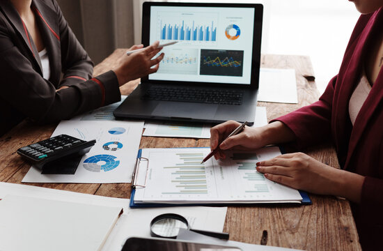 Businesswomen analyzing financial charts and graphs on laptop and documents - Powered by Adobe