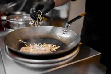 Chef cooking stir-fry in wok with chicken and bean sprouts in a commercial kitchen. Steam rises as fresh ingredients are added, showcasing dynamic food preparation