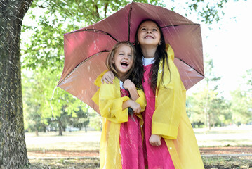Portrait of joyful children spending time outside standing with an umbrella in the rain.