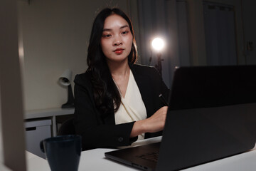 Asian businesswoman working late at night using laptop in dark office