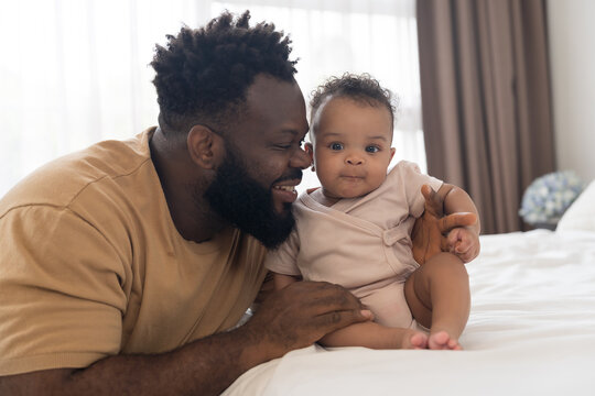 Happy time for African American family. African American father takes care and spends time with his newborn baby on bedroom at home. Infant baby health care with love and kindness - Powered by Adobe