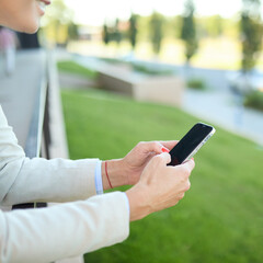 Closeup of a phone and phone screen, young businesswoman woman using a smartphone mobile phone walking down the street, surrounded by moder corporate office buildings